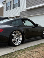 Fiberglass Porsche 997 Mach II side skirts for Carrera/GT3 narrow body, installed on a black car with BetterBodies Motorsport branding